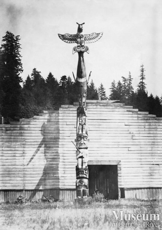 Totem pole in front of big house at Cape Mudge Reserve