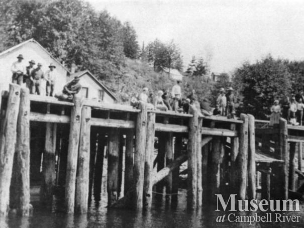 Group of people waving from wharf in front of Quathiaski Cannery
